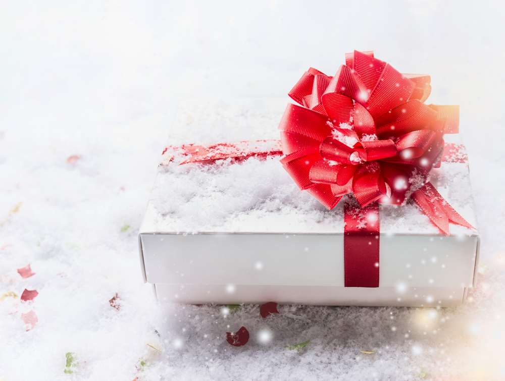 White gift box with red bow on snow with bokeh and snowfall. Copy space for your design: template, invitation, coupon, sale and congratulation