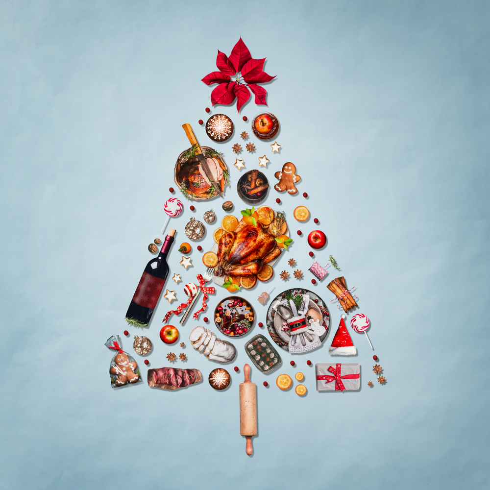 Christmas tree made with various Christmas food: turkey on platter, roasted ham, sweets and candies, cookies , mulled wine, gingerbread  man decorated with gift box and poinsettia on blue background