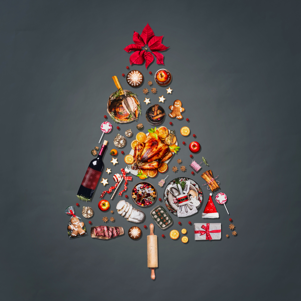 Christmas tree made with various Christmas food: turkey on platter, roasted ham, sweets and candies, cookies , mulled wine, gingerbread  man decorated with gift box and poinsettia on gray background