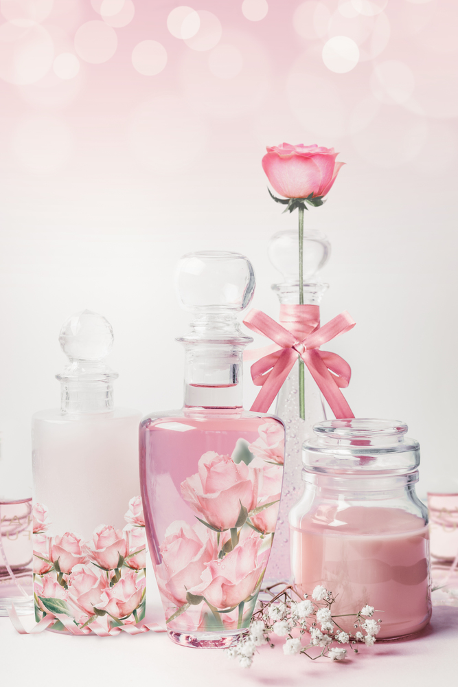 Variety of cosmetic product bottles with roses essence standing on white pink background with bokeh. Skin care, cosmetic shop, sale and abstract beauty concept