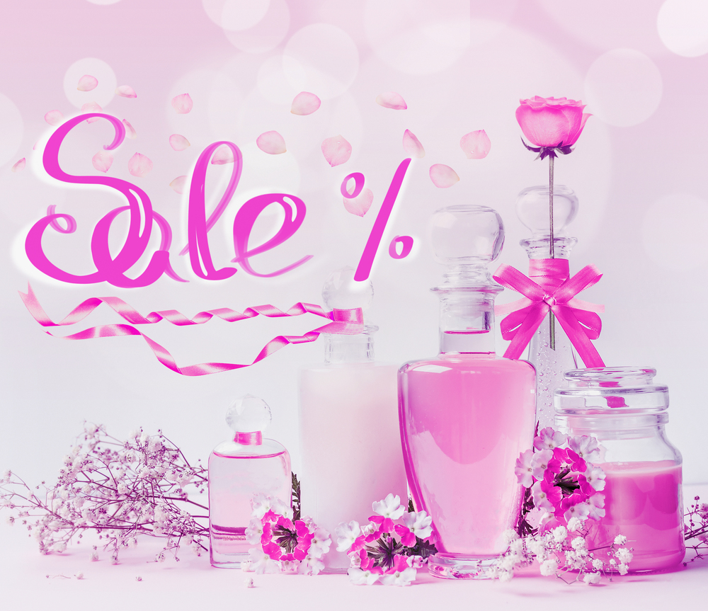 Cosmetic sale text lettering with glass product bottles , pink ribbons and flowers standing on white pink background with bokeh. Skin care, cosmetic shop, sale and abstract beauty concept. Neon color