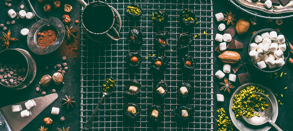 Homemade pralines with dried fruits, nuts and marshmallow. Melted chocolate and cacao powder on kitchen table background with bowls and vintage tools for home patisserie , top view. Sweet food concept