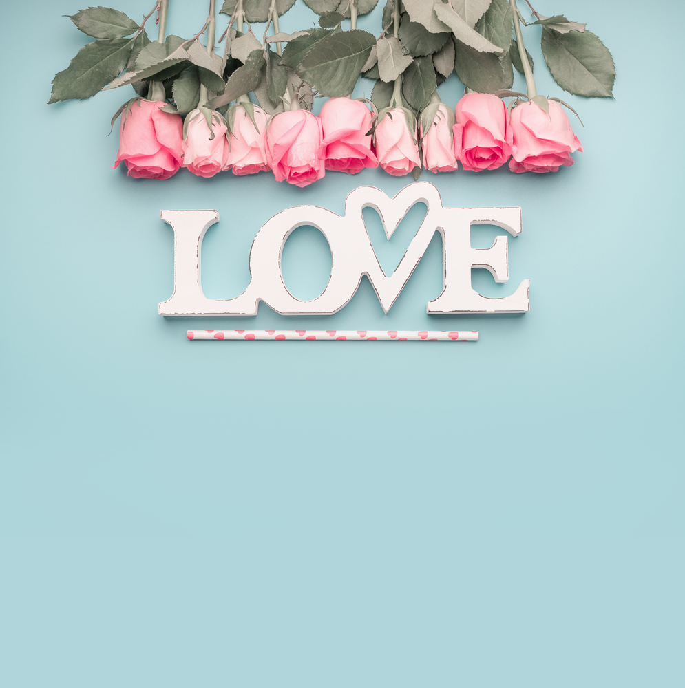 Word love with roses border on pastel blue background, top view with copy space . Valentines day or abstract love concept