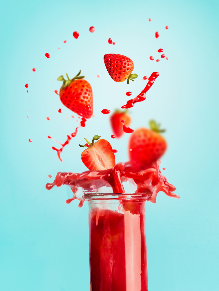 Glass of red strawberry splash summer beverage: smoothie or juice standing at blue background with copy space for your design,recipes and text. Healthy drinks concept