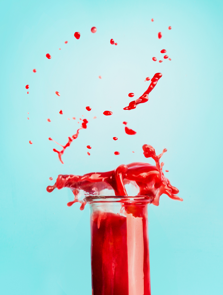 Glass of red splash summer beverage: smoothie or juice standing at blue background with copy space for your design,recipes and text. Healthy drinks concept