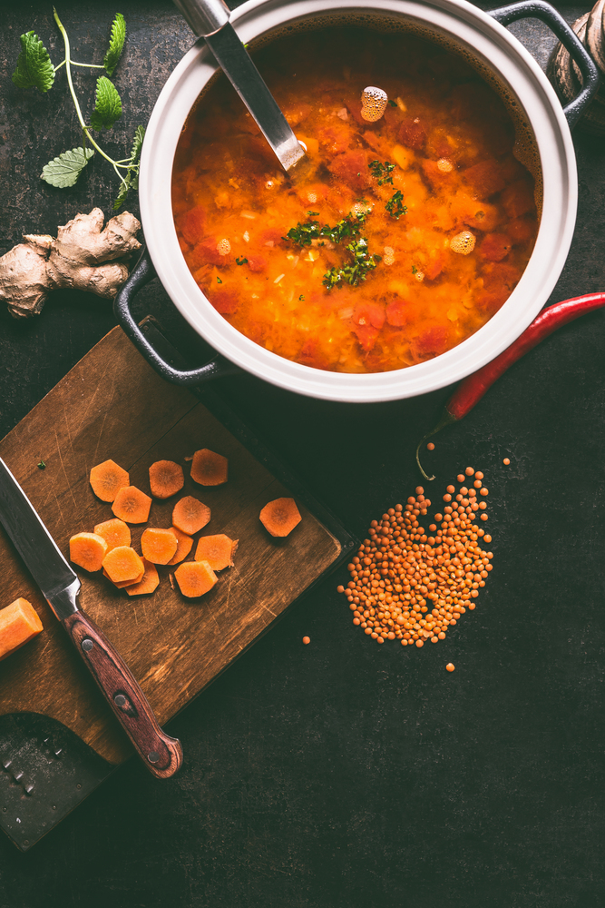 Cooking pot with tasty lentil soup and ladle on dark rustic kitchen table background with ingredients, top view with copy space. Healthy vegan food concept