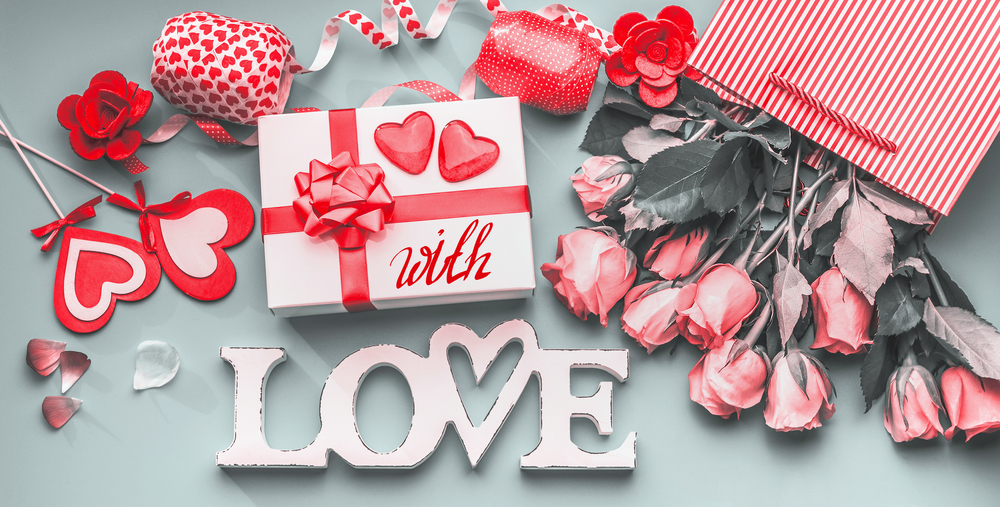 Festive composition of love for Valentines day made with gift box and red bow, shopping bag and roses, hearts and party accessories. With Love message. Flat lay,  View from above