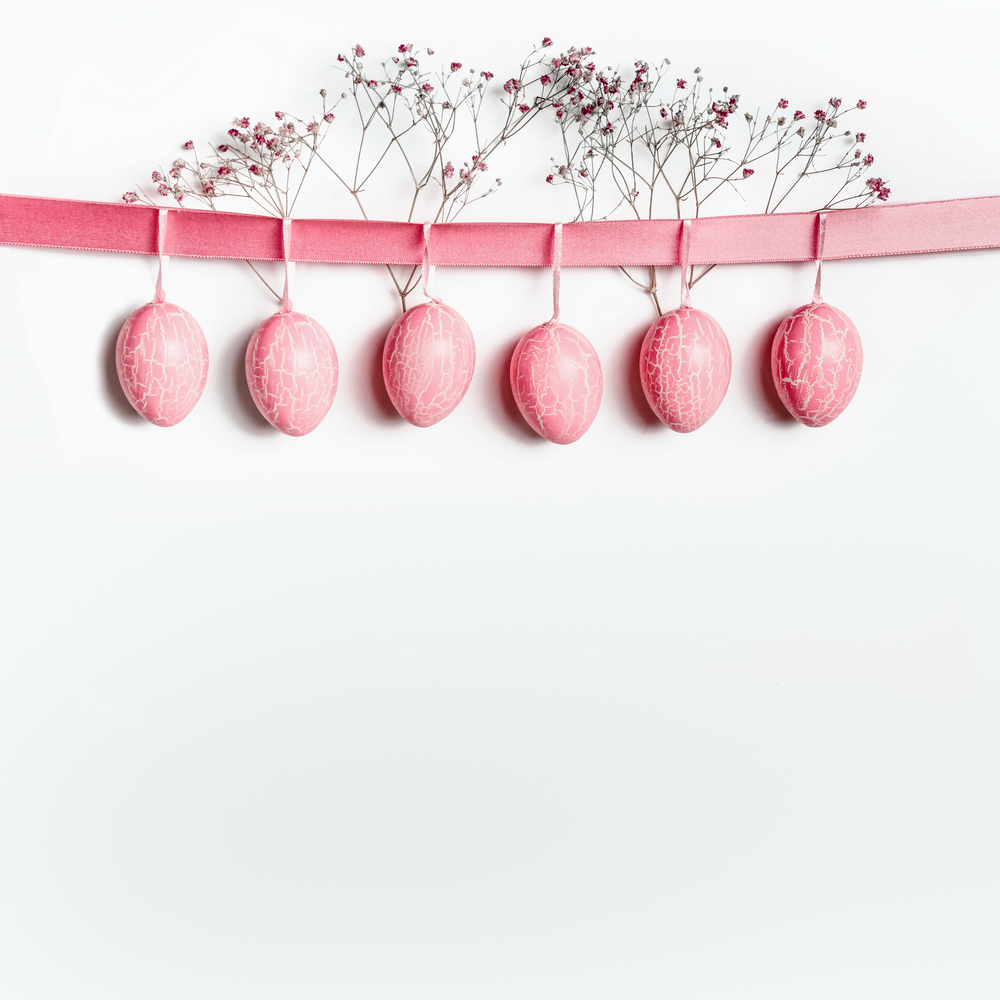 Easter background with hanging pastel pink Easter eggs on ribbon with white flowers. Easter border with copy space for your design