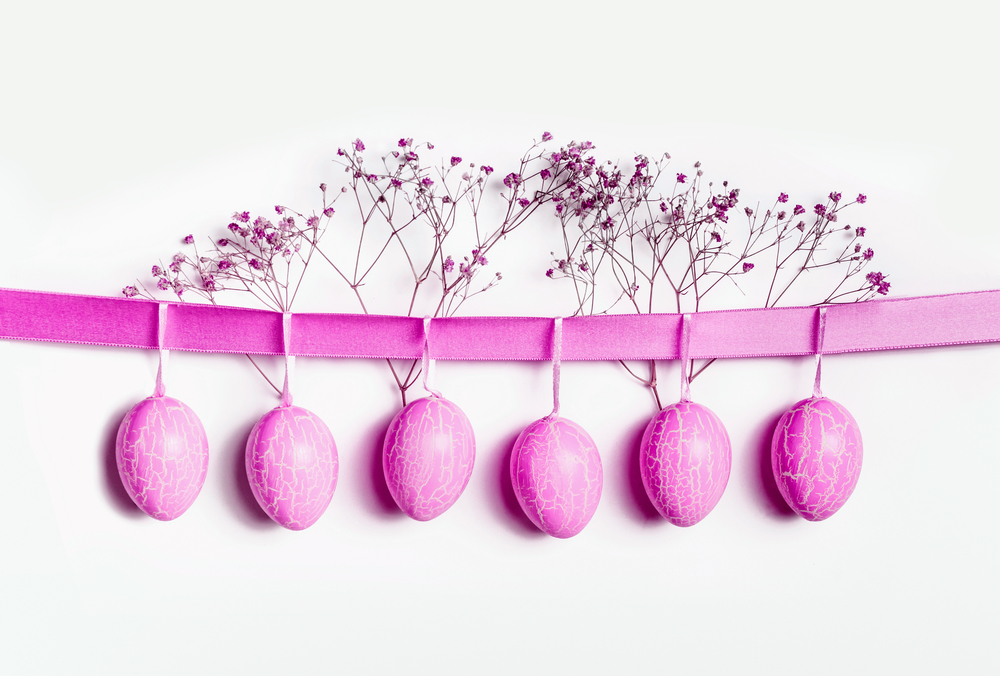 Neon pink Easter eggs hanging at ribbon at white wall background