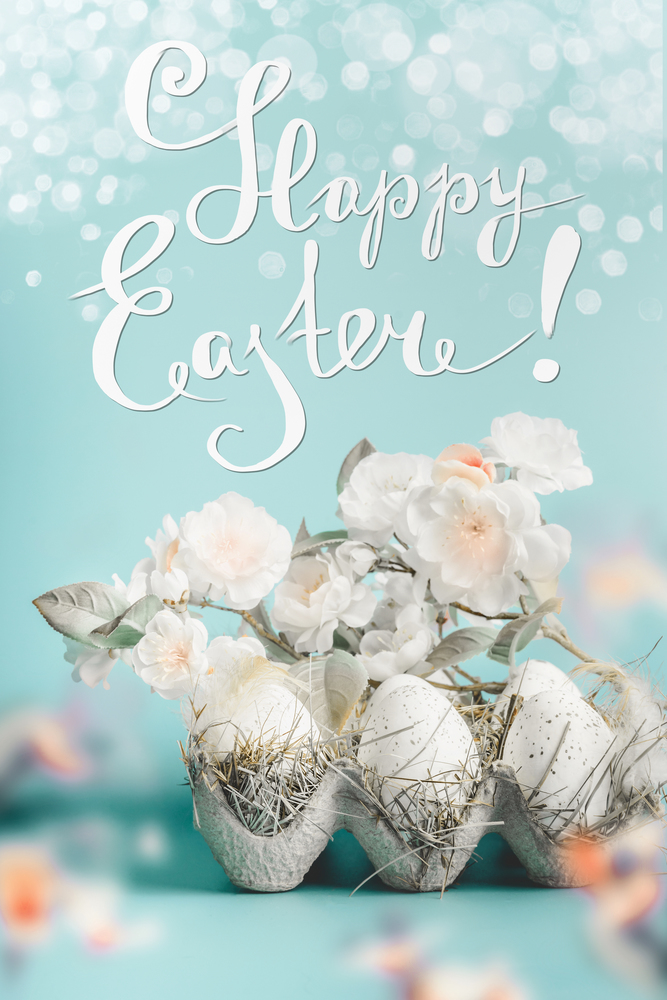 Beautiful Happy Easter greeting card with text lettering. Spring blossom branches and egg-crate with Easter eggs at blue background with bokeh