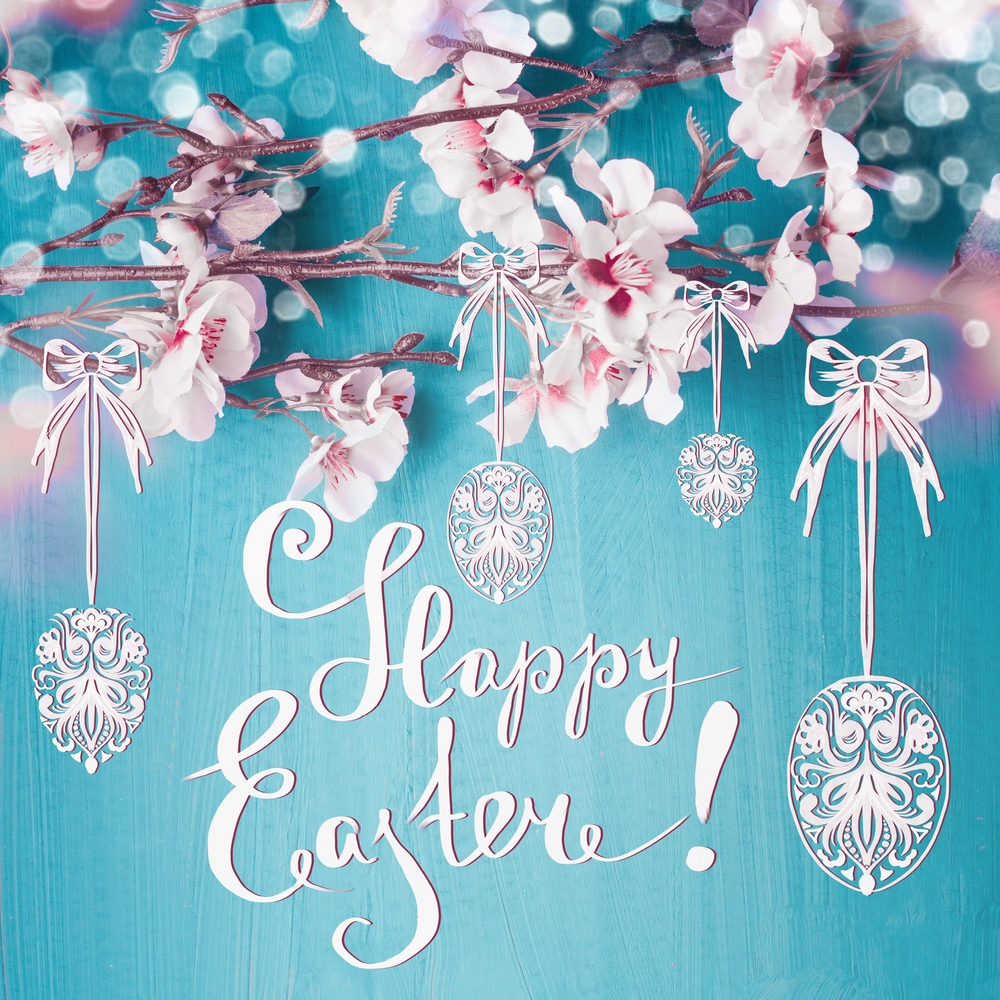 Happy Easter text lettering with spring blossom branches and painted hanging Easter eggs at turquoise blue background. Easter greeting card