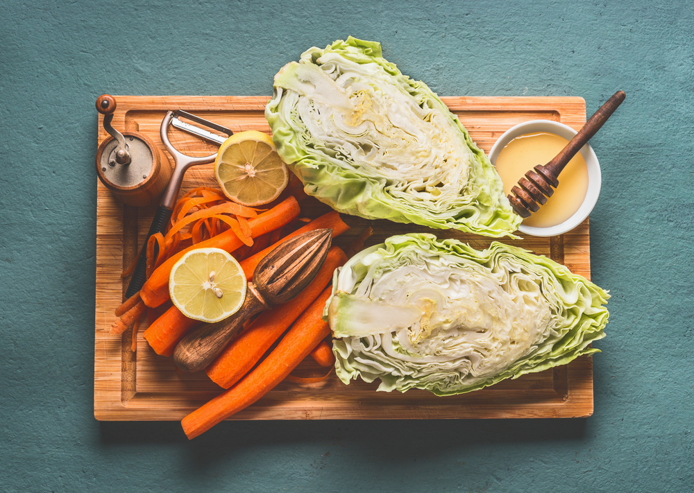 Ingredients for fresh carrot cabbage salad with oil honey dressing in bowl on kitchen table background, top view, with copy space. Vegetarian, low-calorie vegetable eating and weight loss food