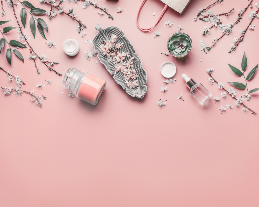 Cosmetic and skin care concept. Various facial anti-aging products on pastel pink background with cherry blossom and leaves, top view, frame. Copy space for your design. Beauty blog layout. Flat lay