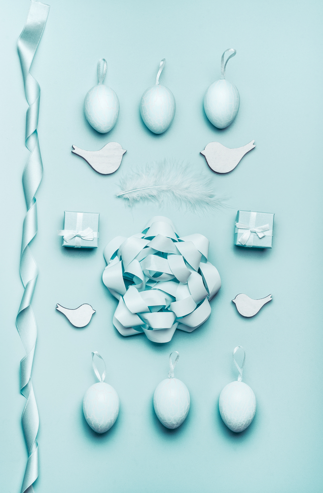 Easter flat lay with eggs, feathers and ribbons at pastel blue background, top view, with copy space for your design. Greeting card