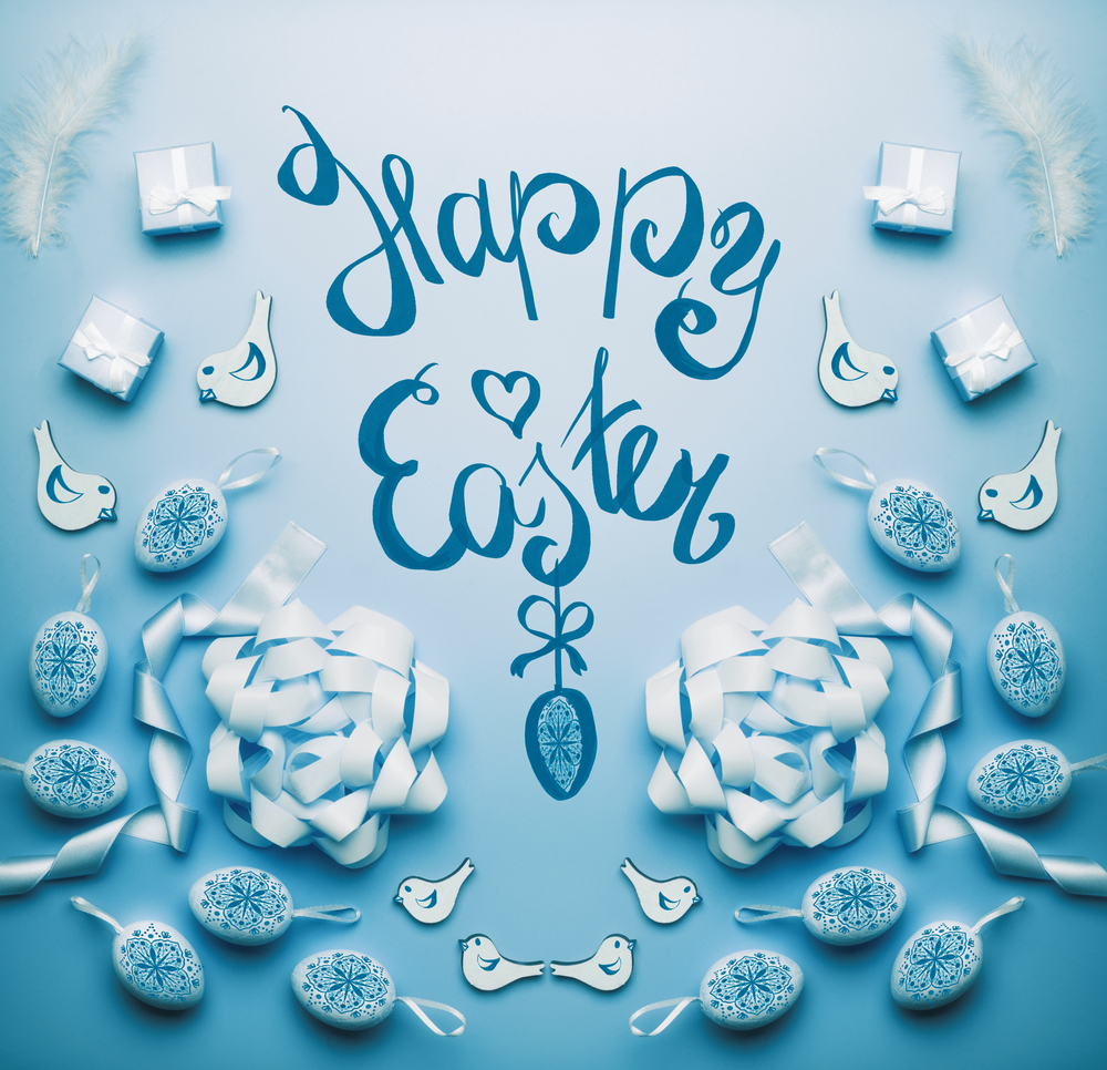Happy Easter card with handwritten text lettering eggs and decoration on blue background, top view, flat lay