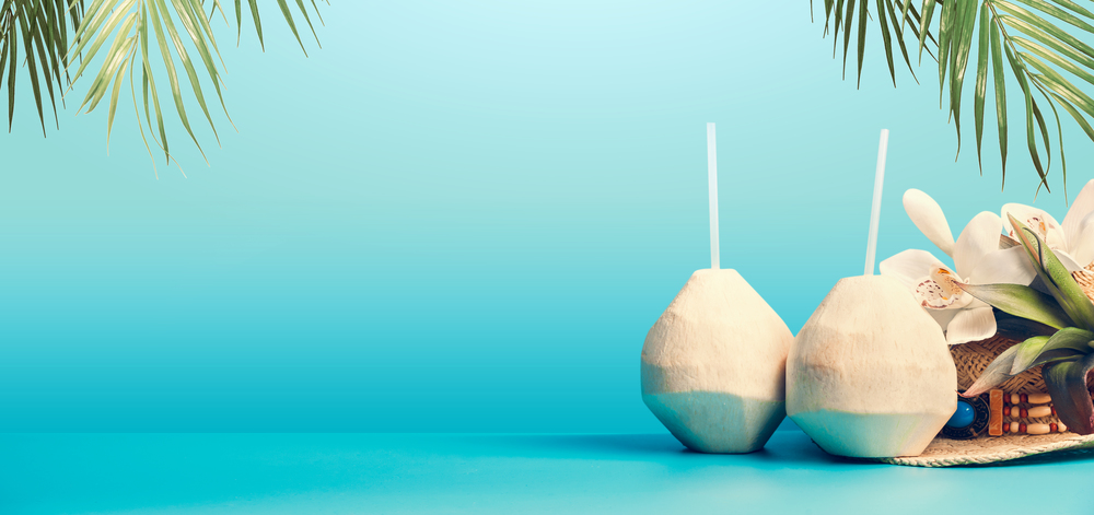 Summer tropical vacation background banner with fresh tropical coconut cocktails , drinking straws and hanging palm leaves on blue turquoise background. Travel and holiday concept