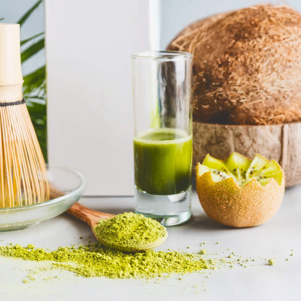 Close up of matcha powder in spoon, matcha espresso on table at light background, front view with copy space. Clean eating, detox beverage, healthy dairy food concept. Antioxidant boost drink