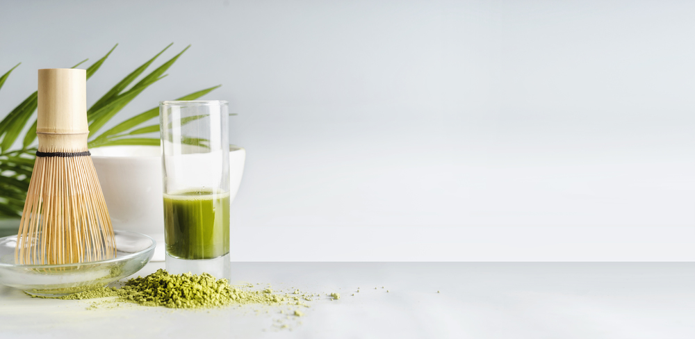 Matcha espresso in glass with whisk on table at light background, front view with copy space. Template or banner.  Clean eating, detox beverage, healthy dairy food concept. Antioxidant boost drink