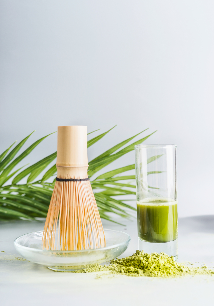 Matcha espresso in glass with whisk and matcha powder on table at light background, front view with copy space. Clean eating, detox beverage, healthy dairy food concept. Antioxidant boost drink