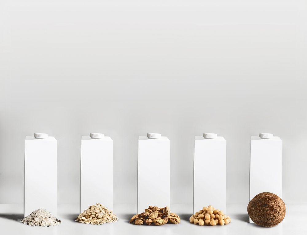 Vegan food concept. Best vegan milk ingredients: rice,  oatmeal, almond, soy and coconut with white blank packaging, tetra-pack,  packet cartons with mock up to branding or design at gray background