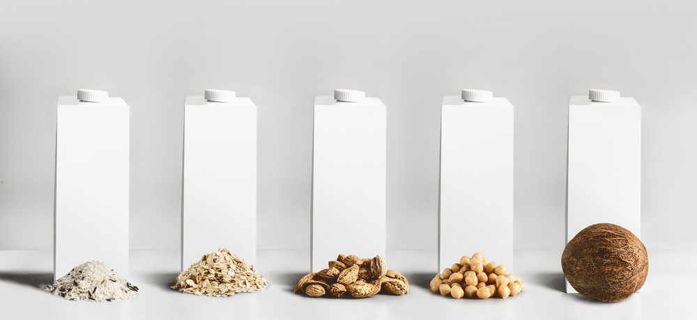 Vegan milk concept. White blank packaging, tetra-pack,  packet cartons with mock up to branding or design with best vegan milk ingredients: rice,  oatmeal, almond, soy and coconut at gray background