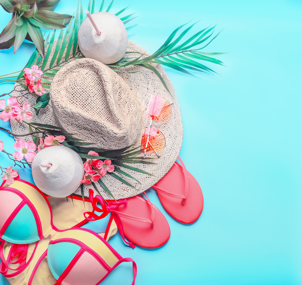 Summer background with top view of woman&rsquo;s summer beach accessories and coconut drinks: bikini,  flip flops, sunglasses, straw hat, palm leaves and tropical flowers on turquoise blue