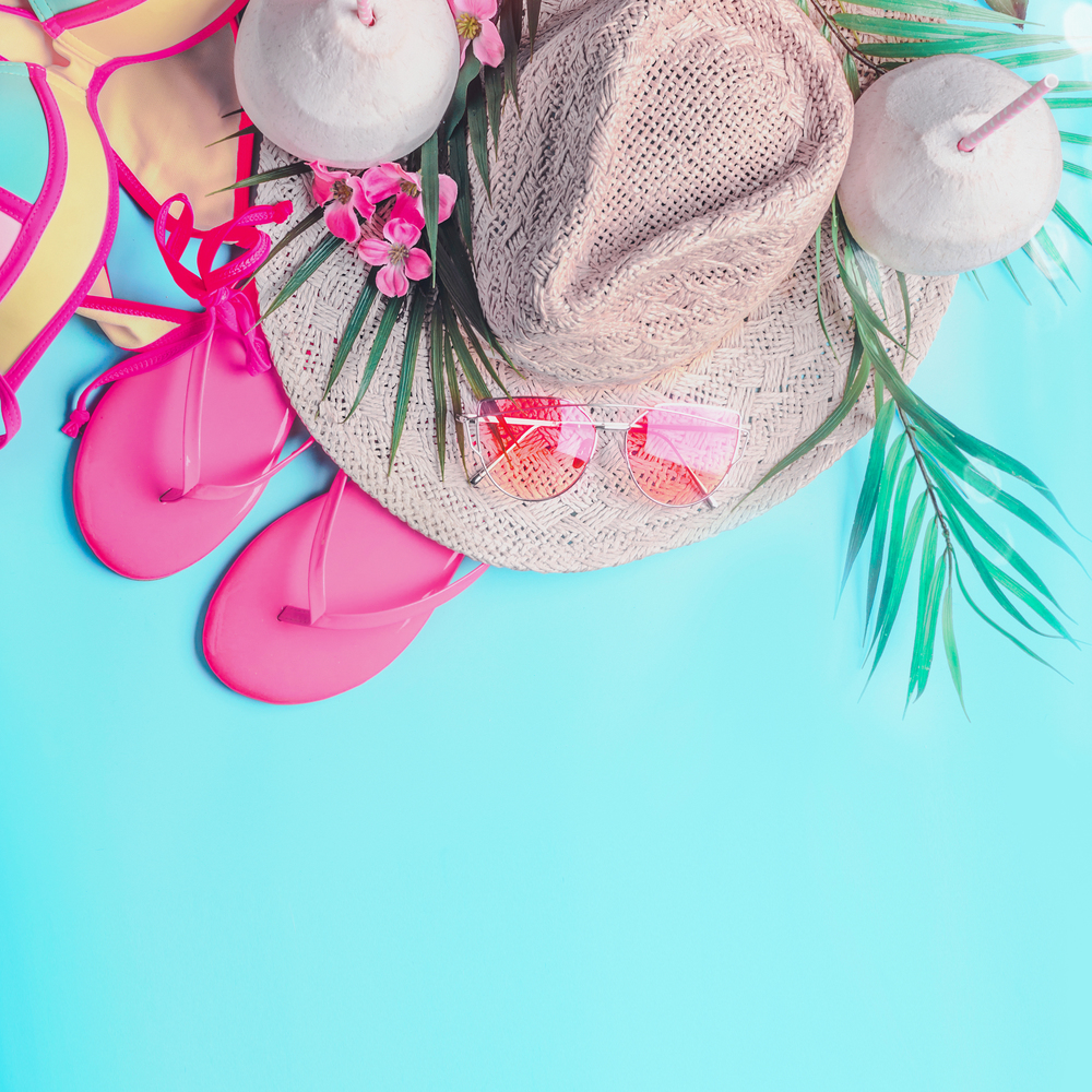 Summer background . Top view of woman&rsquo;s summer beach accessories: bikini,  flip flops, sunglasses, straw hat, palm leaves and tropical flowers on turquoise blue background, banner with copy space