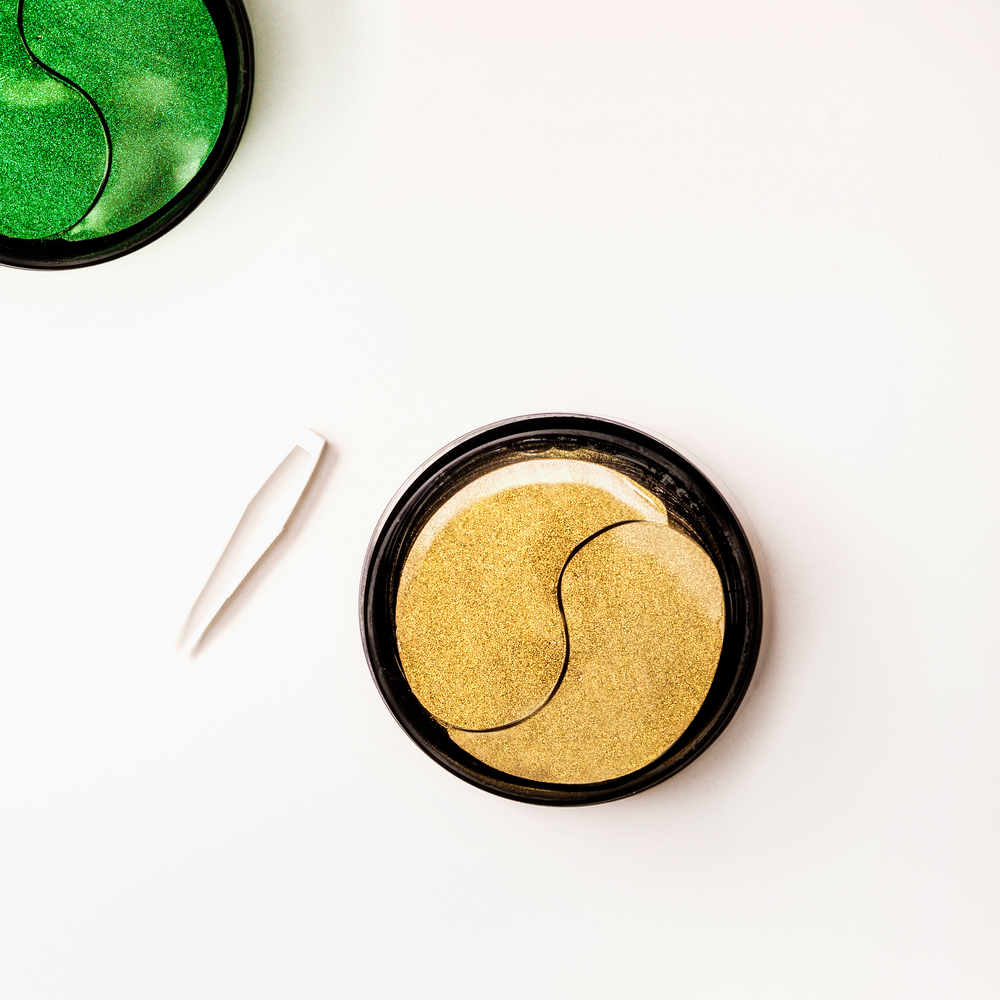Modern cosmetic concept. Golden and green facial eye patches in jar with tweezers. Hydrogel patch.  Anti aging and lifting . Face skin care. Hydrating and wrinkles patch. Top view with copy space