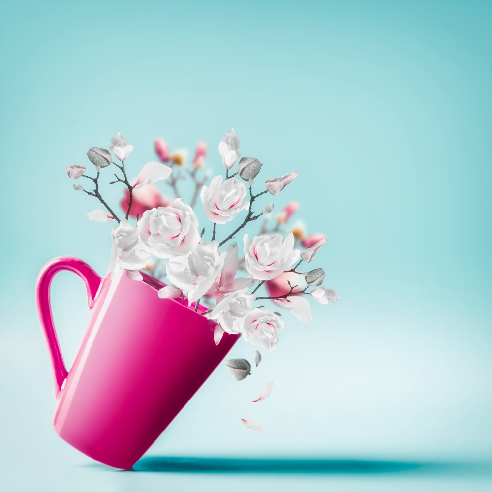 Cup with lovely spring blossom bunch of magnolia and falling petals at light blue background, close up . Flowers arrangement. Valentines, Women&rsquo;s, Wedding Day concept. Vertical. Copy space