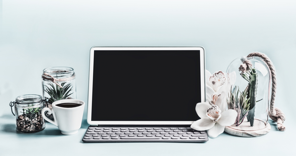 Blank screen modern laptop computer with succulent plants in glasses and orchid flowers on table.  Home female business office workspace.  Black blank screen for your design