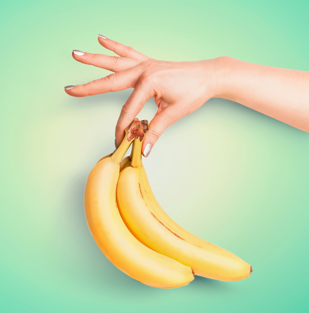 Bunch of organic bananas in female hand at turquoise background. Summer tropical fruits concept. Copy space for your design