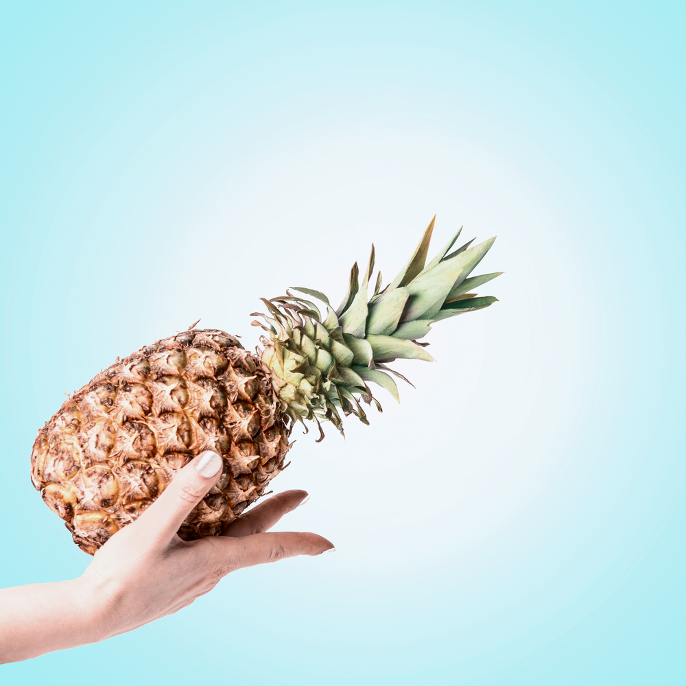 Female hand holding pineapple at light blue background. Summer tropical fruits concept.  Copy space for your design