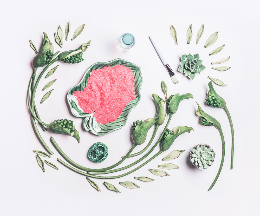 Abstract beauty composing with green tropical leaves and flowers and  bowl with sea salt on white table background, top view, flat lay. Natural skin care, spa and cosmetic concept