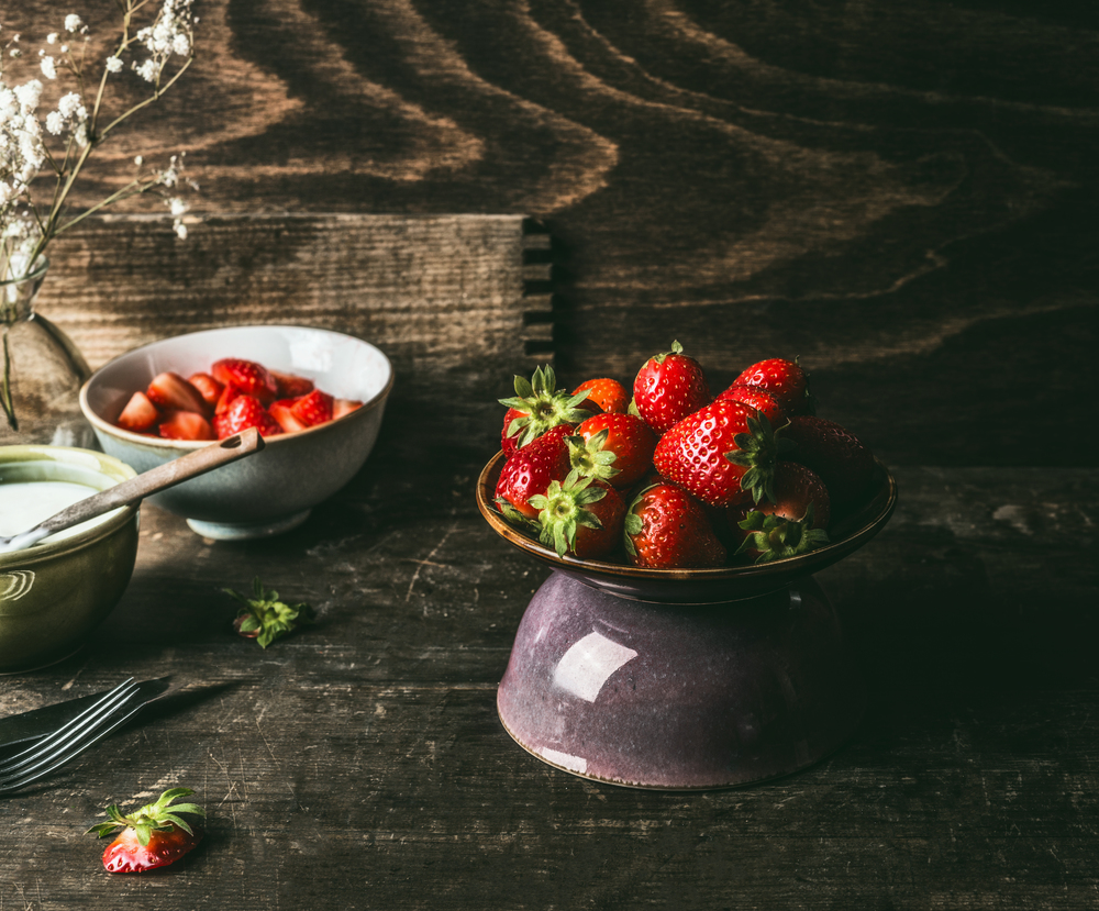 Still life with strawberries bowl on dark rustic kitchen table background
