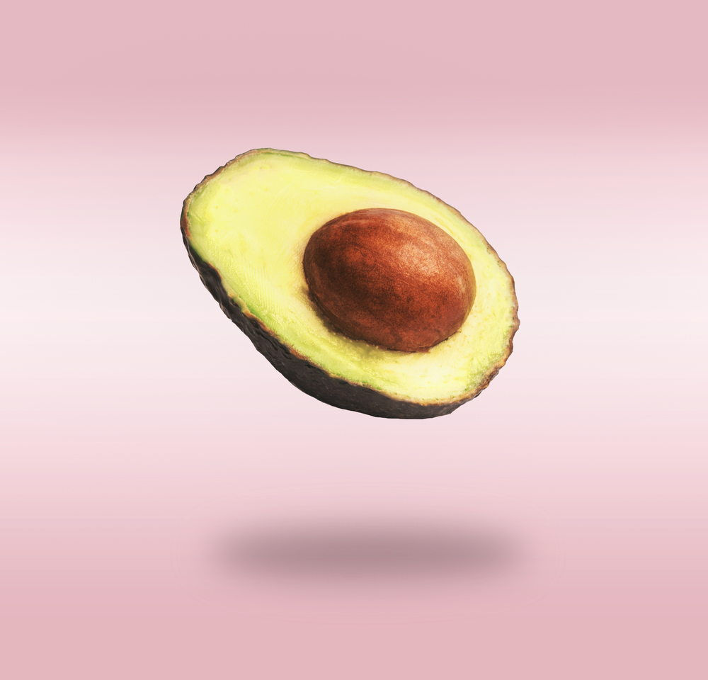 Flying half avocado with seed at pink background with shadow. Concept of food levitation