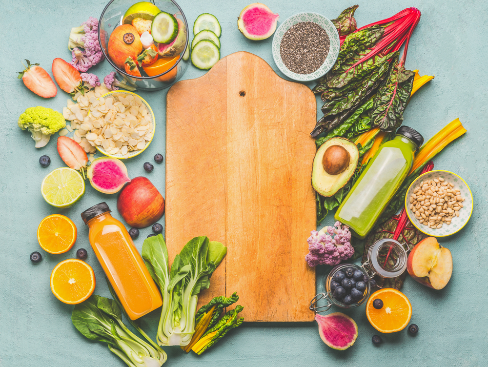 Healthy smoothie ingredients around wooden cutting board, top view. Summer food and beverages background. Vegan superfood: Fruits, berries and vegetables, chia seeds, almond, pine nuts. Detox concept