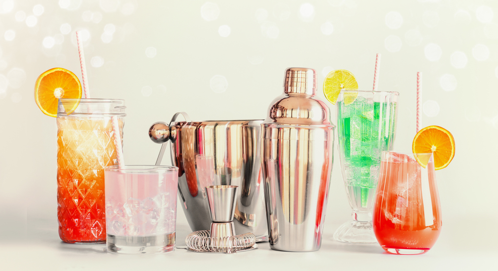 Colorful summer long drinks bar and cocktails tools in various glasses with drinking straws and citrus fruits standing at light background