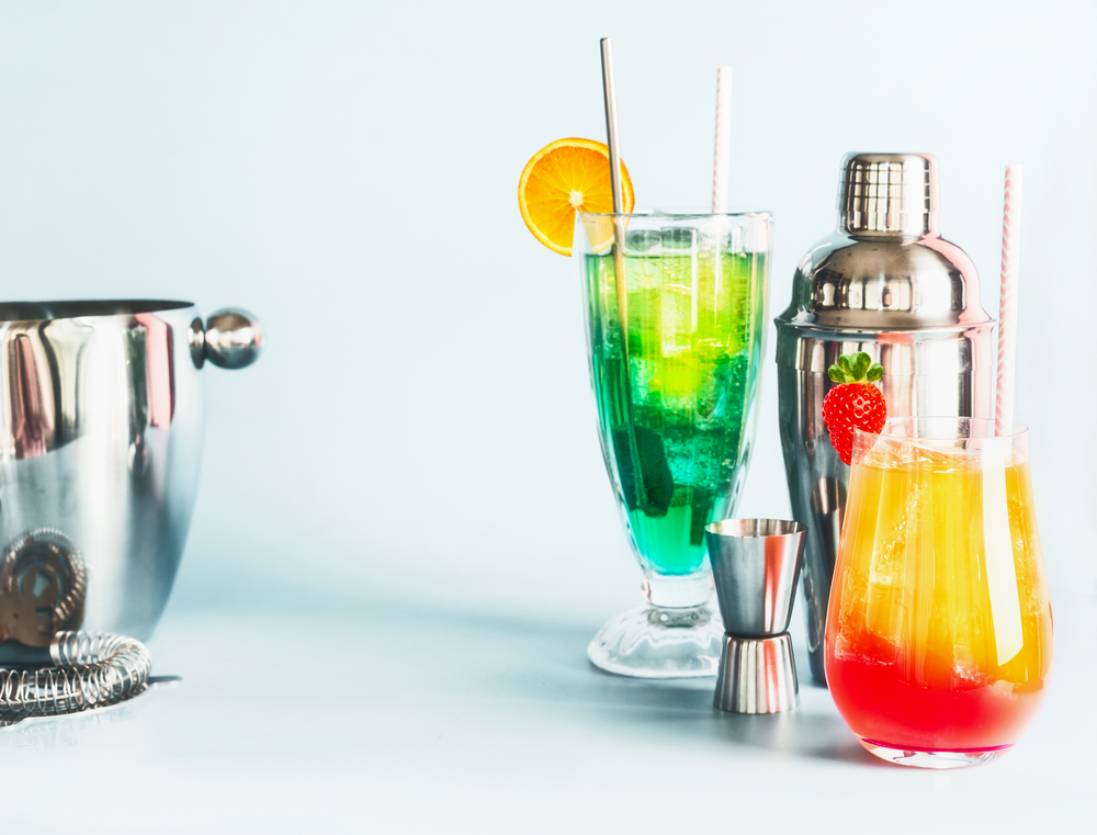 Various  colorful long drinks and cocktails bar tools at light blue background, copy space. Summer alcoholic beverages