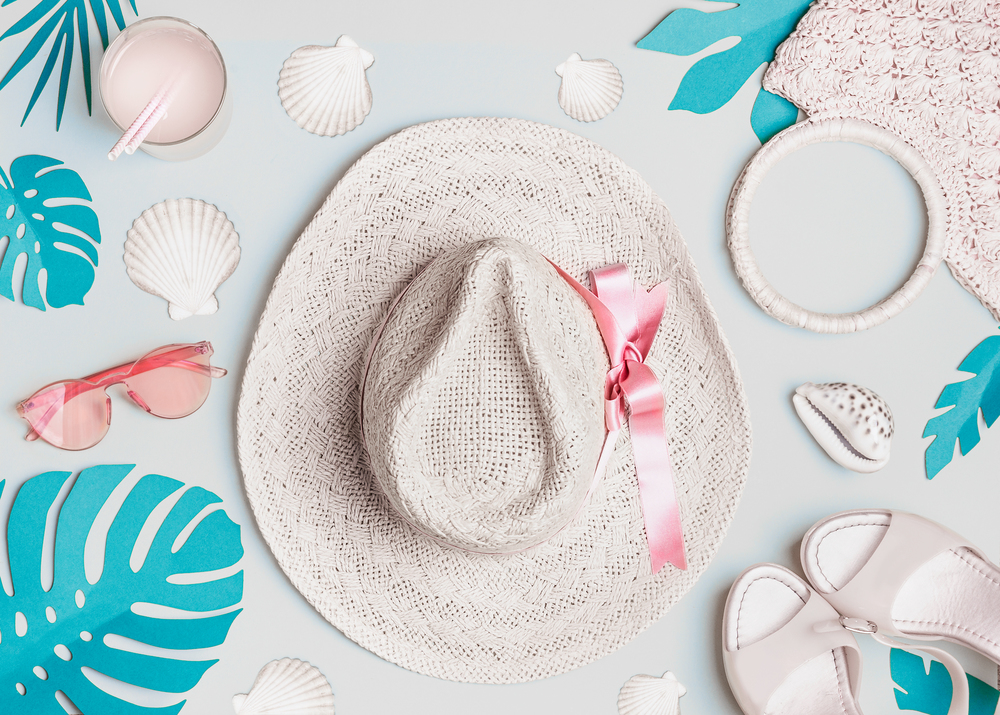 Summer woman accessories with  shells and tropical leaves on pastel color background, top view. Straw hat, sunglasses, sandals and handbag. Holiday vacation. Female fashion outfit