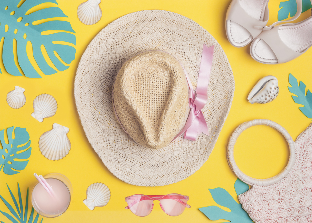 Summer flat lay. Beach accessories with  shells and tropical leaves on yellow background, top view. Straw hat, sunglasses, sandals and handbag. Summer holiday vacation. Female fashion outfit