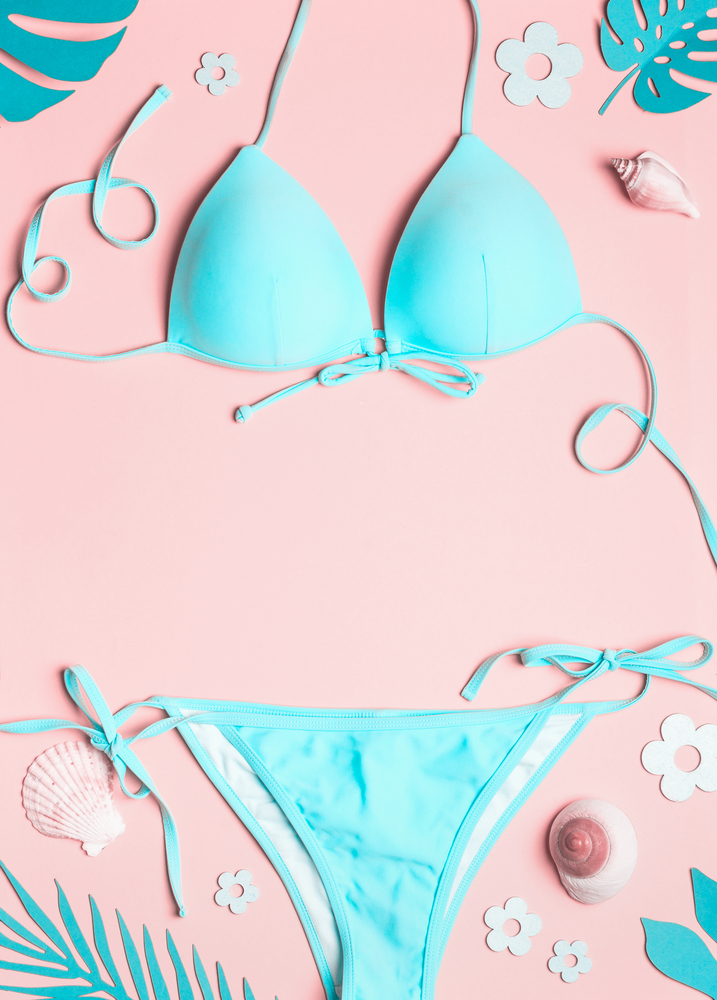 Turquoise blue bikini with shells and tropical leaves on pastel pink background, top view. Flat lay. Copy space. Frame. Summer holiday vacation.