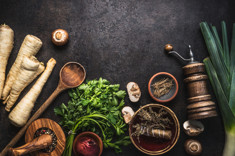 Rustic food background with parsley root vegetables, herbs,spices ,leek and champignon mushrooms on dark rustic table with kitchen utensils, top view. Copy space. Vegetarian food