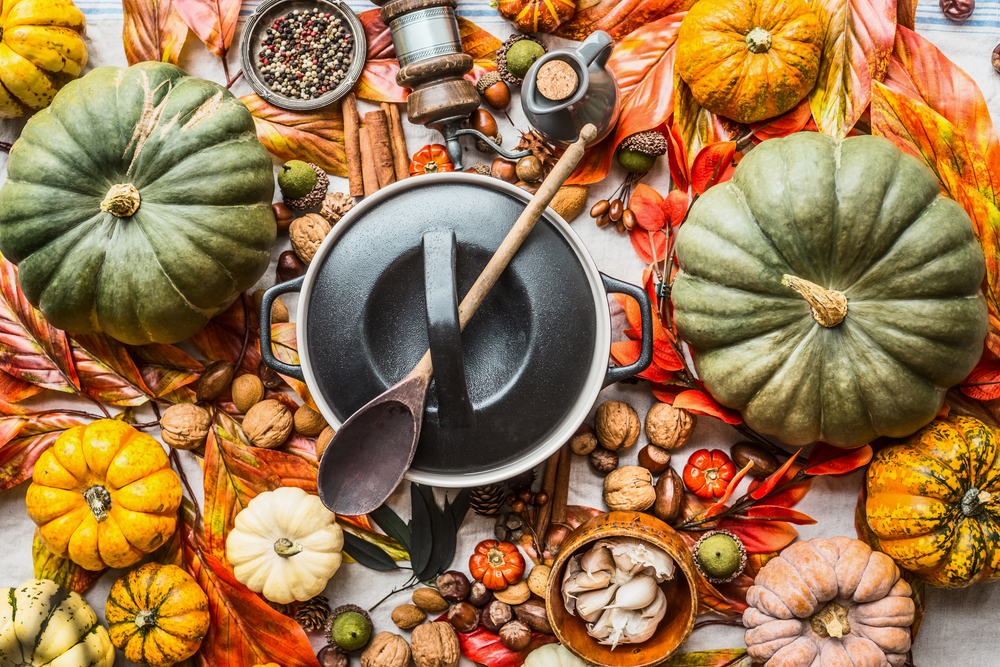 Various colorful organic pumpkins and cooking pot with spoon on kitchen table with nuts , spices and autumn leaves, top view. Autumn still life with pumpkins. Thanksgiving recipes. Flat lay. Seasonal