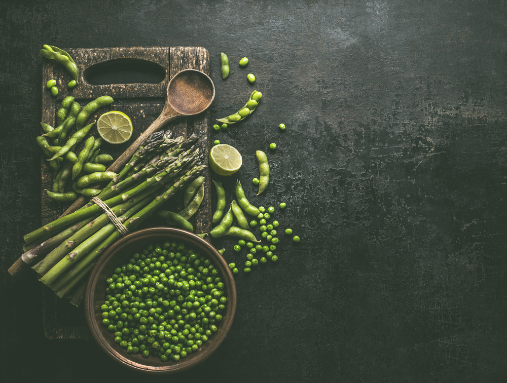 Green asparagus with edamame soybeans, lime and green peas on dark rustic kitchen table background, top view. Copy space. Healthy vegetarian food . Green cooking ingredients.