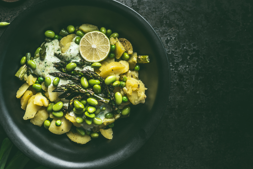 Close up of potatoes and green asparagus salad with edamame soybeans in black bowl, top view with copy space. Healthy vegetarian food concept