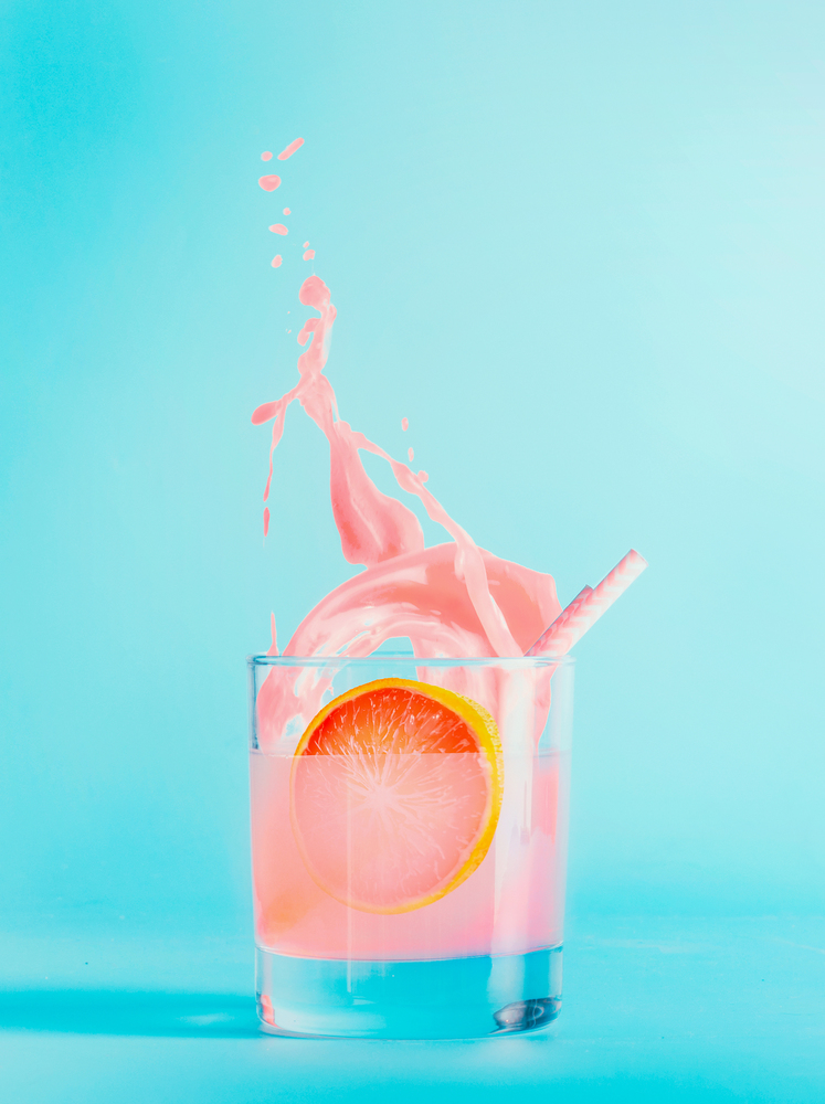 Splash of grapefruit drink in glass on blue background. Summer refreshing beverage . Pink grapefruit lemonade or juice