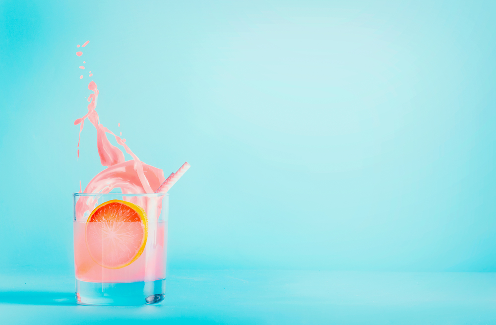 Grapefruit drink in glass with splash on blue background. Summer refreshing beverage . Pink grapefruit lemonade . Copy space