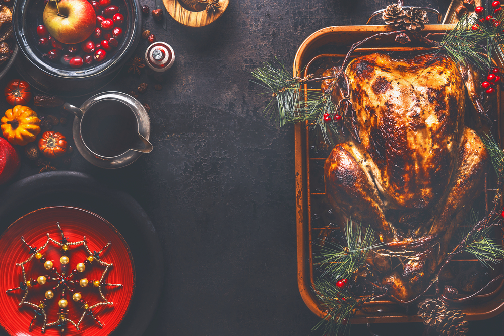 Christmas dinner background. Roasted stuffed turkey served with fresh cranberries, pine branches and sauce on rustic background with red plate, snowflakes decoration, apple and little pumpkins.