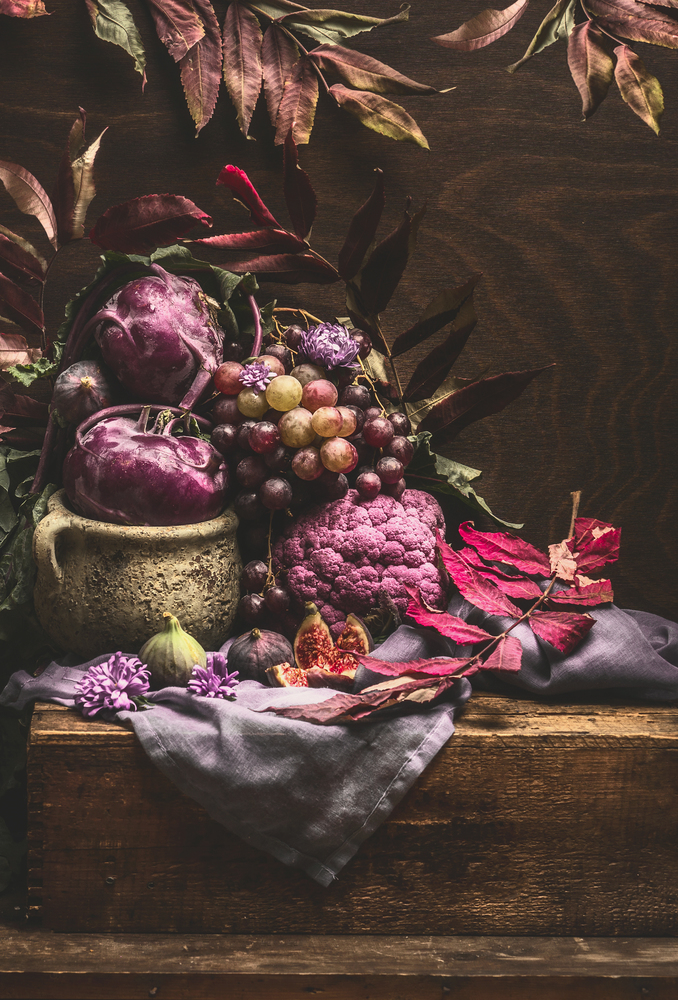 Still life with purple fruits and vegetables on wooden table with crockery, napkin and autumn leaves . Copy space for your design