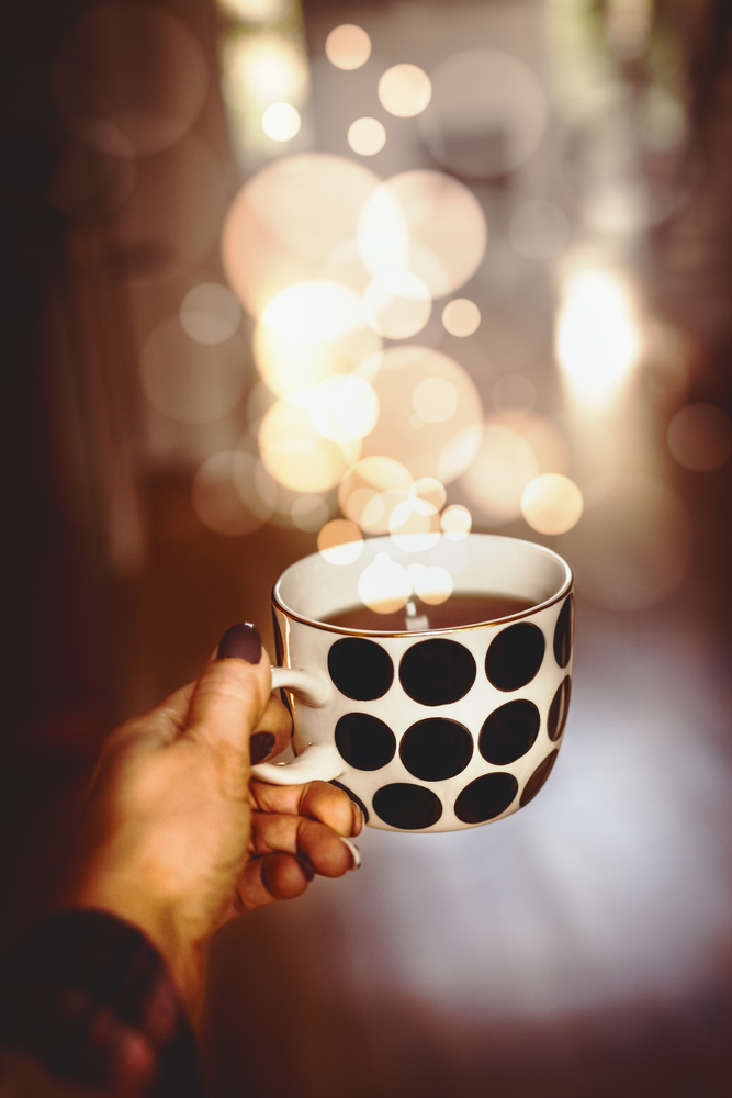 Female hand holding polka dot mug with hot drink and bokeh